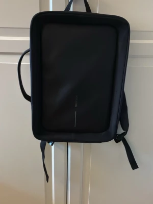 Svart ryggsäck från XD Design - Snygg svart ryggsäck från XD Design med minimalistisk och modern look. Väskan har en rektangulär form, diskret logga på framsidan och bärhandtag upptill. Tillverkad i slitstarkt material. Perfekt för laptop och vardagsprylar! I fint skick.