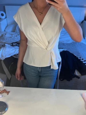 Vit topp Zara - Snygg vit omlottopp med knyt i sidan och v-ringad hals. Toppen har korta ärmar och en avslappnad passform som ger en chic och enkel look. Perfekt att matcha med jeans för en clean stil.