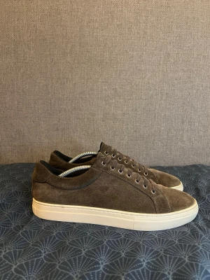 Bruna mockasneakers från Vagabond  - Snygga sneakers i brun mocka med klassisk låg profil och vita gummisulor. Skorna har matchande bruna skosnören och diskreta sömmar för en clean look. Perfekta för dig som gillar stilrena och tidlösa sneakers. 
