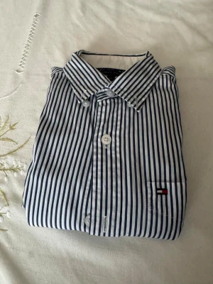 Randig skjorta från Tommy Hilfiger - Snygg skjorta från Tommy Hilfiger med marinblå och vita ränder. Klassisk krage, knappar framtill och liten logga på bröstfickan. Tillverkad i mjuk bomull för en bekväm känsla och stilren look.