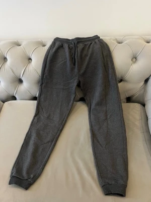 Mörkgrå mjukisbyxor från Koton Kids - Säljer ett par mörkgrå mjukisbyxor från Koton Kids med resår och dragsko i midjan samt ribbade muddar vid bensluten. Storlek 11-12 år eller 146-152 cm 