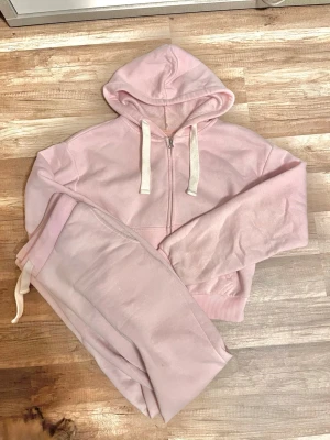 Ljusrosa mjukisset med hoodie från Gina Tricot - Mysigt loungewear-set i ljusrosa med matchande hoodie och byxor. Hoodien har dragkedja, vita snören och ribbade muddar. Byxorna har resår i midjan och snörning. Perfekt för chill dagar hemma.  Nästan aldrig använd och i mycket bra skick. Skriv innan köp är villig att diskutera pris💕