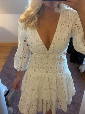 Vit klänning med v-ringning - Supersnygg vit klänning i virkad spets med djup v-ringning och trekvartsärmar. Klänningen har markerad midja, utsvängd kjol och fina virkade detaljer över hela plagget. Perfekt för dig som gillar boho-stil och vill sticka ut.