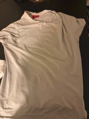 Vit t-shirt från HUGO - Klassisk vit t-shirt från HUGO med enkel och stilren design. T-shirten har korta ärmar och rund halsringning. Tillverkad i mjukt bomullsmaterial som känns skönt mot huden. Perfekt basplagg för alla tillfällen.