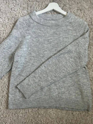 Ljusgrå stickad tröja - Mysig ljusgrå stickad tröja med rund halsringning och ribbade muddar vid ärmslut och nederkant. Fint skick men har ett litet hål i sig på baksidan som man kan se på de 2 sista bilderna (syns knappt när man har på sig den)                     Storlek M men är rätt liten i storlek💞