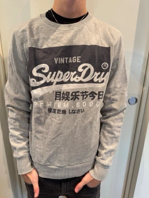 Grå Superdry Sweatshirt  - Säljer en riktigt fet Superdry Sweatshirt i storlek S. Modellen är 180 cm och väger 65 kg.