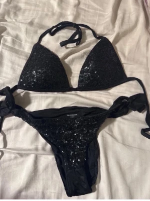 Svart bikini med paljetter Calzedonia - Snygg svart bikini från Calzedonia med glittrande paljetter på både överdel och underdel. Bikinin har trekantsmodell på toppen och knyt i både nacke och sidor. Väldigt fint skick! Knappt använd. 