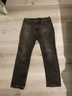 Grå jeans från Lee, modell West - Säljer ett par grå jeans från Lee, modell West. Jeansen har klassisk femficksdesign, raka ben och normal midja. Tillverkade i bomull med en snygg tvättad finish som ger en avslappnad look.