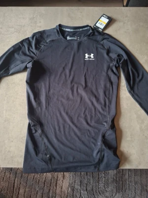 Svart långärmad träningströja UA - Svart långärmad compression tröja från Under Armour, köpt på gymgrossisten för 500 (inkl frakt/450 exkl). Helt ny och lappen är kvar