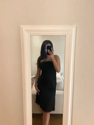 Svart axelbandslös klänning - Säljer en svart, axelbandslös klänning med figurnära passform. Klänningen har en enkel och stilren design med lätt vågig kant nertill. Klänningen består av två lager vare sig översta är meshtyg. Perfekt för dig som gillar minimalistisk stil och vill ha en klassisk look. Den är väldigt stretchig och kan passa S-M beroende på vad för passform man letar efter.