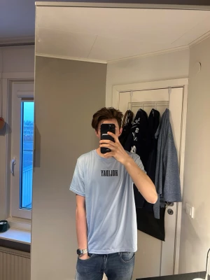 Ljusblå t-shirt med tryck Holiday - Ljusblå t-shirt med texten 'HOLIDAY' på bröstet och ett stort färgglatt tryck av palmer och solnedgång på ryggen. Avslappnad passform och rund halsringning. Perfekt för dig som gillar chill vibes och snygga prints. Väldigt bra skick andvänd ett par gånger och passar perfekt nu till sommaren som är runt hörnet ☀️⛱️