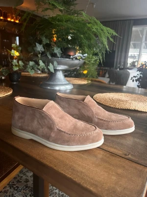 Bruna mocka Loro piana loafers - Säljer ett par stilrena Loro piana loafers i brun mocka med vit, något upphöjd gummisula. Skorna har en klassisk slip-on design utan snörning och en mjuk, rundad tå. Perfekta nu inför sommar och för dig som gillar en avslappnad men ändå snygg look. Ingår tyvärr ingen box. Skriv vid frågor eller funderingar!☺️