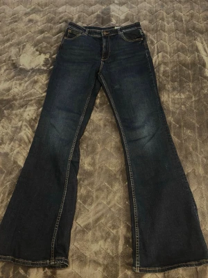 Mörkblå bootcut jeans - Säljer ett par mörkblå bootcut jeans med klassiska fem fickor och kontrastsömmar. De är helt oanvända! 