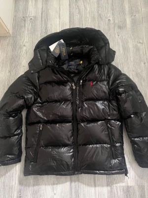 Ralphlauren jacka - Hej! En glossy Ralph lauren jacka till salu. Jackan är i jättebra skick och den har inga defekter elller tecken av användning. Jackan är köpt på Nk och kvittot finns kvar. Jag säljer jackan pågrund av att den tyvärr inte passar mig, priset kan diskuteras lite vid snabbaffär. hör av dig vid frågor 😁