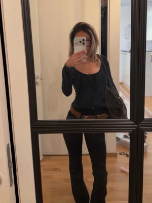 Svart långärmad topp med ribbad detalj - Säljer en svart långärmad topp med ribbad struktur och djup rundringning. Toppen har en slim passform och är tillverkad i ett stretchigt material som sitter snyggt på kroppen. Perfekt att styla med jeans eller kjol.