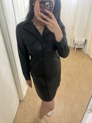 Svart skjortklänning i skinnimitation - Säljer en stilren svart klänning/långskjorta i mjukt konstläder från det svenska märket Carin Wester i storlek 42 (XL). Funkar utmärkt som en Skjortjacka (midiklänning, vardagsklänning). Absolut, helt ny.   Nypris: 600kr  Märke: Carin Wester Storlek: 42 = XL Skick: Helt ny/ aldrig använd med prislapp! Pris: 499kr