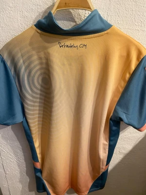 Manchester City matchtröja Puma - Säljer en Manchester City matchtröja från Puma i snyggt beige och blått med klubbmärke och Etihad Airways-tryck på bröstet. Tröjan har korta ärmar, krage och är tillverkad i ett lätt, ventilerande funktionsmaterial. Perfekt för fotboll eller träning.