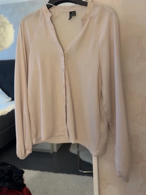 Beige blus med v-ringning - Stilren beige blus från H&M med v-ringning och knäppning framtill. Blusen har långa ärmar och är tillverkad i ett mjukt, tunt tyg som ger ett avslappnat fall. Perfekt att matcha med jeans eller kjol för en enkel men snygg look.