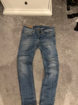 Dondup jeans - Säljer ett par blå slim fit jeans från Dondup med klassisk femficksdesign och snygga slitningar framtill. Jeansen har normal midja, knappgylf och är tillverkade i ett mjukt denimtyg med stretch.