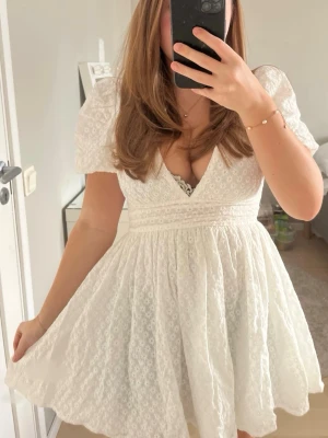 Vit kortklänning från Hello Molly - Superfin vit kortklänning från Hello Molly med djup v-ringning, puffärmar och markerad midja med en rosett man knyter där bak. perfekt för studenten 🤍 Helt ny endas testad en gång med lappen kvar, säljer då jag bestämt mig för en annan🤍original pris: 1200kr med frakt