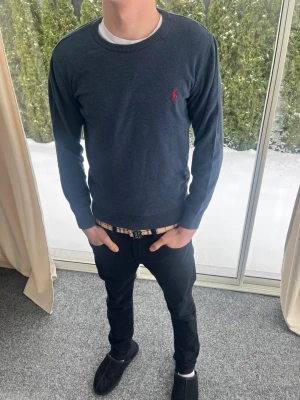 Mörkblå stickad tröja Polo Ralph Lauren - Mörkblå stickad tröja från Polo Ralph Lauren med rund halsringning och den klassiska röda logotypen broderad på bröstet. Strl S. Personen på bilden är 183 cm lång