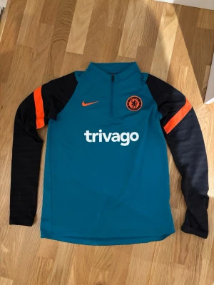Chelsea träningströja - En snygg blå svart och orange träningströja från Chelsea/nike. Den har varma ärmar och fungerar när man tränar, när man är hemma eller någon annan stans också. Tveka inte att fråga vid fundering. (Äkta tröja)