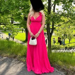 Skrikrosa balklänning - Säljer en chockrosa långklänning/ balklänning med djup v-ringning, volangdetaljer och superfin öppen rygg med snörning. Fin rosa/ skrikrosa färg. Passar S/M. Använd en gång på min bal🩷