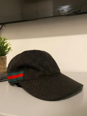 Svart keps från Zara  med GG-mönster - Snygg svart keps från Zara  med diskret GG-monogram över hela kepsen. På sidan finns det klassiska gröna och röda bandet som ger en lyxig känsla. Justerbar rem baktill för perfekt passform. Perfekt accessoar för att lyfta din outfit.