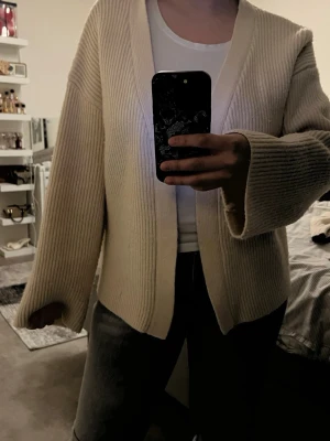 Beige ribbstickad kofta - Säljer en oversized beige ribbstickad kofta med breda ärmar och öppen front. Koftan är mjuk och har en avslappnad passform, perfekt att slänga över en t-shirt. Passar dig som gillar minimalistisk och stilren look.