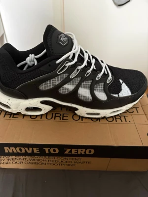 Nike tn - Snygga svarta Nike sneakers med vit sula och specklade detaljer. Ovandelen är i mesh och syntet med vita snören och coola transparenta paneler på sidorna. Stora vita swoosh-loggor på sidan ger en sportig vibe. Perfekta för dig som gillar streetwear och modern design.