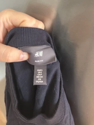 Mörkblå slim fit tröja från H&M - En stilren mörkblå tröja från H&M i slim fit-modell. Tröjan har rund halsringning, långa ärmar och ribbade muddar vid ärmslut och nederkant. Perfekt för dig som gillar en enkel och klassisk look.