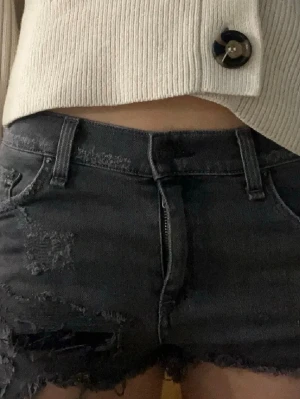 Svarta jeansshorts med slitningar - Oanvända men köpta secondhand💓 Säljer ett par svarta jeansshorts med råa kanter och slitna detaljer. Shortsen har fem fickor, bälteshällor och dragkedja med knapp. Perfekta för en avslappnad och trendig look.