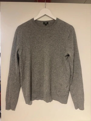 Grå stickad tröja från Uniqlo Kashmir  - Säljer en stilren grå stickad tröja från Uniqlo med rund halsringning och svarta armbågslappar. Tröjan har lång ärm och ribbade muddar vid ärmslut och nederkant. Perfekt till höst och vinter för en enkel men snygg look.