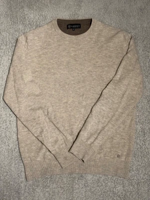 Stickad tröja Lagency - Klassisk beige stickad tröja från Lagency med rund halsringning och ribbade muddar vid ärmslut och nederkant. Tröjan är enkel och stilren, perfekt för lager på lager och passar till det mesta. Materialet känns mjukt och bekvämt.