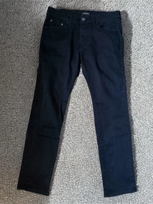 Svarta slim jeans från Jack & Jones - Snygga svarta slim fit jeans från Jack & Jones, modell Glenn. Perfekt för dig som vill ha ett par svarta stilrena jeans. Midjan är 41cm och längden är 97cm.