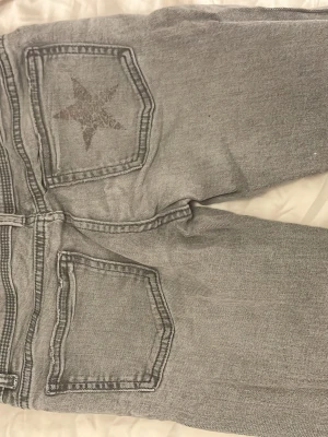 Grå jeans med stjärna på bakfickan - Säljer ett par grå jeans i klassisk femficksmodell med en cool stjärndetalj på ena bakfickan. Jeansen har raka ben och är lowwaist