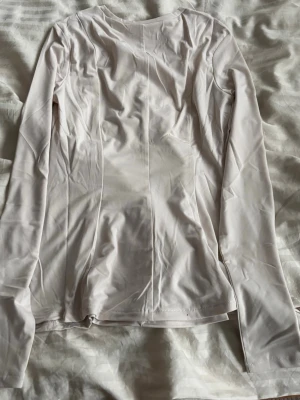 Ljusbeige långärmad topp H&M - En stilren ljusbeige långärmad topp från H&M. Toppen har en figurnära passform och är tillverkad i ett mjukt, stretchigt material som känns skönt mot huden. Perfekt att matcha med jeans eller kjol för en clean look.