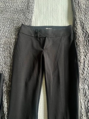 Svarta leggings från Nelly - Säljer ett par svarta leggings från Nelly med låg midja och knappdetaljer framtill. De har en tight passform och är tillverkade i ett stretchigt material som sitter snyggt på kroppen. Perfekta till både oversized tröjor och crop tops!