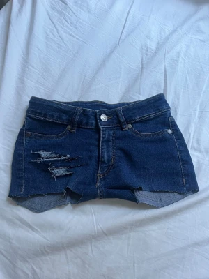 Mörkblå lågmidjade jeansshorts med kors detalj - säljer dessa jättefina blåa lowrise shorts, har sytt ett kors på bakfickan ! så snygga shorts men passar tyvärr inte mig längre ☹️ bakfickan är fortfarande användbar! ställ frågor ! priset kan alltid diskuteras 💛  stl 24/25 så passar xxs/och kanske xs! stretchig!