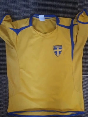 Sverige fotbollströja Ibrahimovic #10 - Gul och blå fotbollströja med Sveriges landslagsemblem på bröstet och Ibrahimovic samt nummer 10 tryckt på ryggen. Tröjan har korta ärmar och är tillverkad i ett lätt, ventilerande material som passar perfekt till träning eller match.