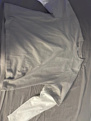 Grå långärmad t-shirt från Bershka - Säljer en stilren grå långärmad t-shirt från Bershka. Tröjan har en enkel design med rund halsringning och är tillverkad i mjuk bomull. Perfekt för en avslappnad look och lätt att matcha med andra plagg.