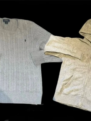 2 Ralph Lauren tröjor  - Kabelstickad tröja i ljusgrått från Polo Ralph Lauren. Klassisk rund halsringning, ribbade muddar och diskret broderad logga på bröstet. Perfekt för dig som gillar stilrena och tidlösa plagg. Materialet känns mjukt och håller värmen bra.