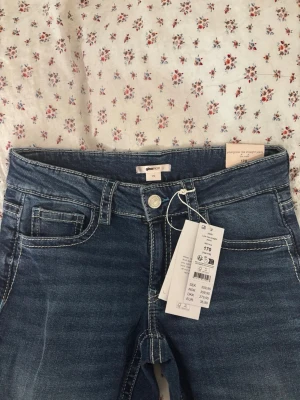 Blå straight jeans från Gina Tricot - Säljer ett par blå straight jeans från Gina Tricot med slitningar på benen och vita kontrastsömmar. Storlek 170. Klassisk femficksmodell och låg midja. Jeansen har en snygg tvättad look och är i mjukt denimtyg. Perfekta till en avslappnad stil.