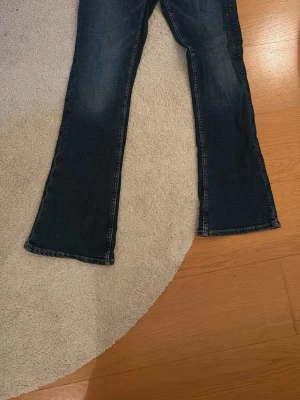 Mörkblå bootcut jeans Gina Tricot - Snygga mörkblå bootcut jeans från Gina Tricot. Jeansen har en klassisk femficksmodell och lätt utsvängda ben. Perfekta för dig som gillar en retrostil och vill ha ett par jeans som sticker ut lite extra.