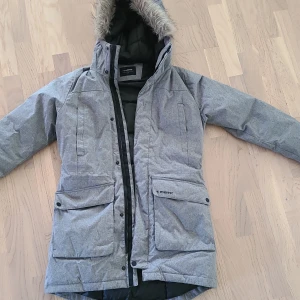 Parkas Everest  - Säljer en grå parkajacka från Everest med huva och fuskpäls. Jackan har stora fickor framtill, dragkedja och knappar, samt svart quiltat innerfoder. Perfekt för kalla dagar och snygg till vardagslooken.