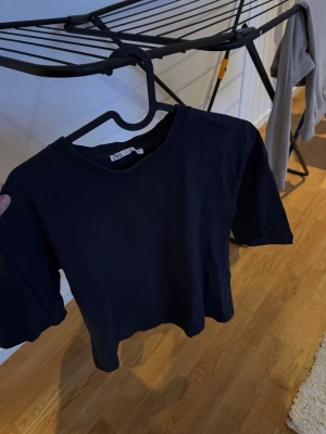 Svart croppad t-shirt från ARKET - En stilren svart croppad t-shirt från ARKET med rund hals och korta ärmar. Perfekt till jeans eller kjol för en enkel och clean look. Tillverkad i mjuk bomull som känns skön mot huden.