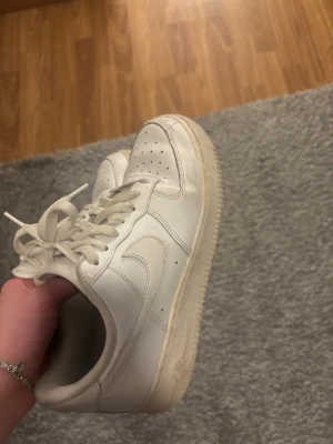 Vita Nike Air Force 1 sneakers - Klassiska vita Nike Air Force 1 sneakers i läder med perforerad tå, vit sula och snörning. Ikonisk swoosh på sidan och låg modell som passar till det mesta. Perfekta för dig som gillar streetwear och tidlös stil. Priset kan diskuteras skicka gärna förslag!