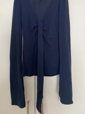 Marinblå långärmad knytblus - Trendig marinblå långärmad blus med djup v-ringning och knyt framtill. Perfekt att styla med höga jeans för en cool look. Är från gina tricot, men är helt slutsåld. Den är i nyskick. Skriv vid frågor💕