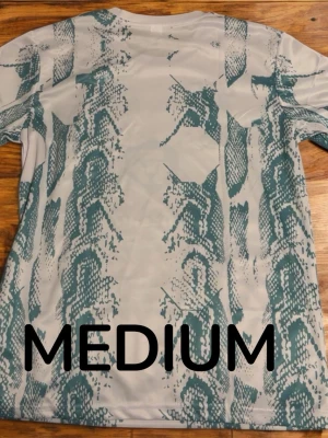 UFC x Venum vit tränings-tshirt - Snygg vit UFC tränings-tshirt från Venum med grönt ormmönster och tryck från crypto.com. T-shirten har rund hals, korta ärmar och sportig passform. Perfekt för gymmet eller kampsportsträning. OBS kan kännas mindre för den är compressed