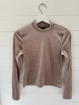 Beige sammetsmjuk långärmad tröja - Mysig långärmad tröja i beige sammetstyg med rak passform och enkel design. Perfekt för lager-på-lager och ger en soft känsla. Tröjan har en liten ståkrage och är stretchig för extra komfort.